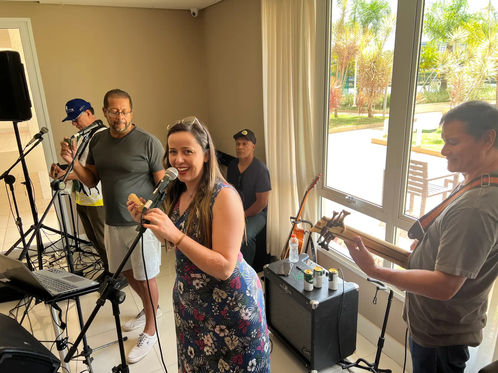 Cantora sorrindo ao microfone, com a banda atrás, numa sala clara, em festa de aniversário.