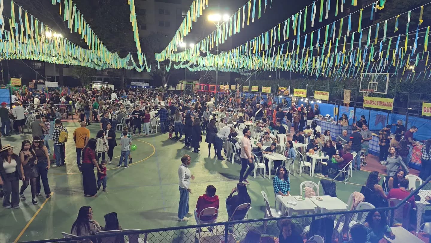 Quadra lotada sob bandeirolas verdes e azuis, com gente dançando.